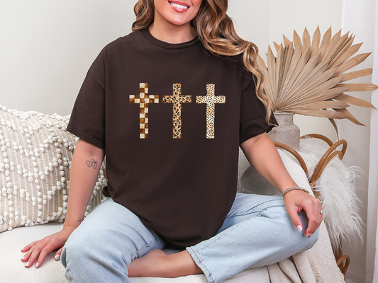 Woman wearing brown three crosses Christian graphic tee with leopard, checkerboard and dotted cross designs