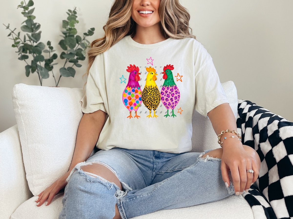 Woman wearing a natural-colored graphic tee featuring three bright patterned chickens