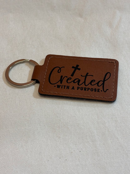 Brown rectangular keychain with stitched edges, engraved with a cross and “Created With a Purpose.”