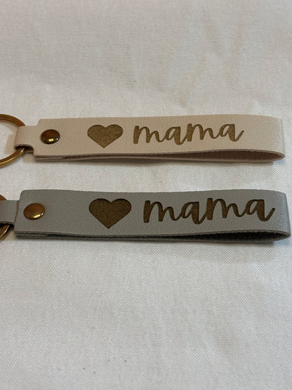 Cream and gray wristlet keychains engraved with a heart and “mama” script, finished with gold-tone hardware.