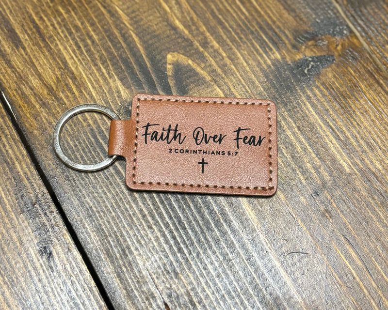 Brown leather keychain with 'Faith Over Fear' text on a wooden surface