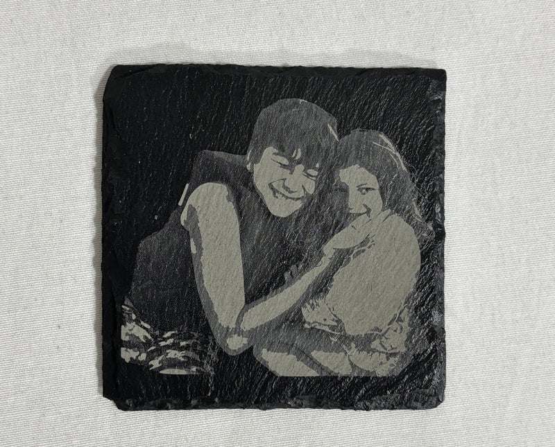 Engraved stone with a black and white illustration of two people embracing on a textured surface.