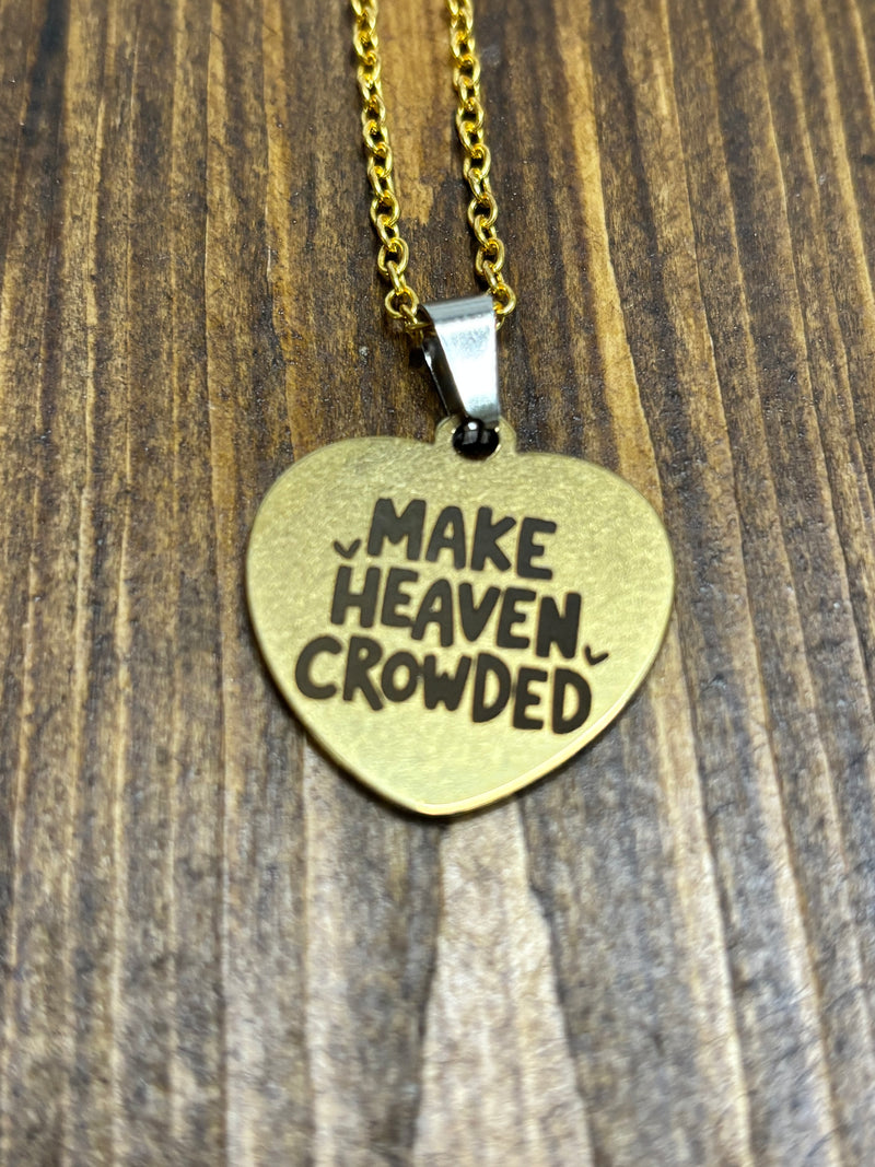 Heart-shaped brass pendant with 'MAKE HEAVEN CROWDED' text on a wooden surface