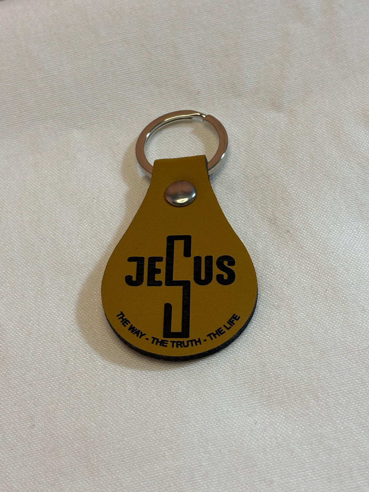 Mustard teardrop keychain engraved with a stylized “Jesus” design and “The Way - The Truth - The Life.”