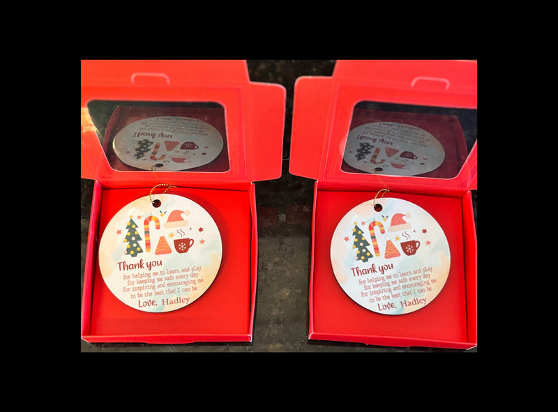 Two ceramic ornaments with Christmas designs and text in red gift boxes.