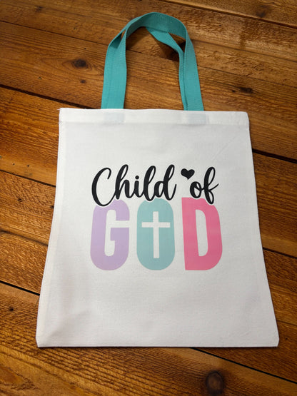 White canvas kids tote bag with teal handles and “Child of God” lettering in purple, mint, and pink with a cross in the O