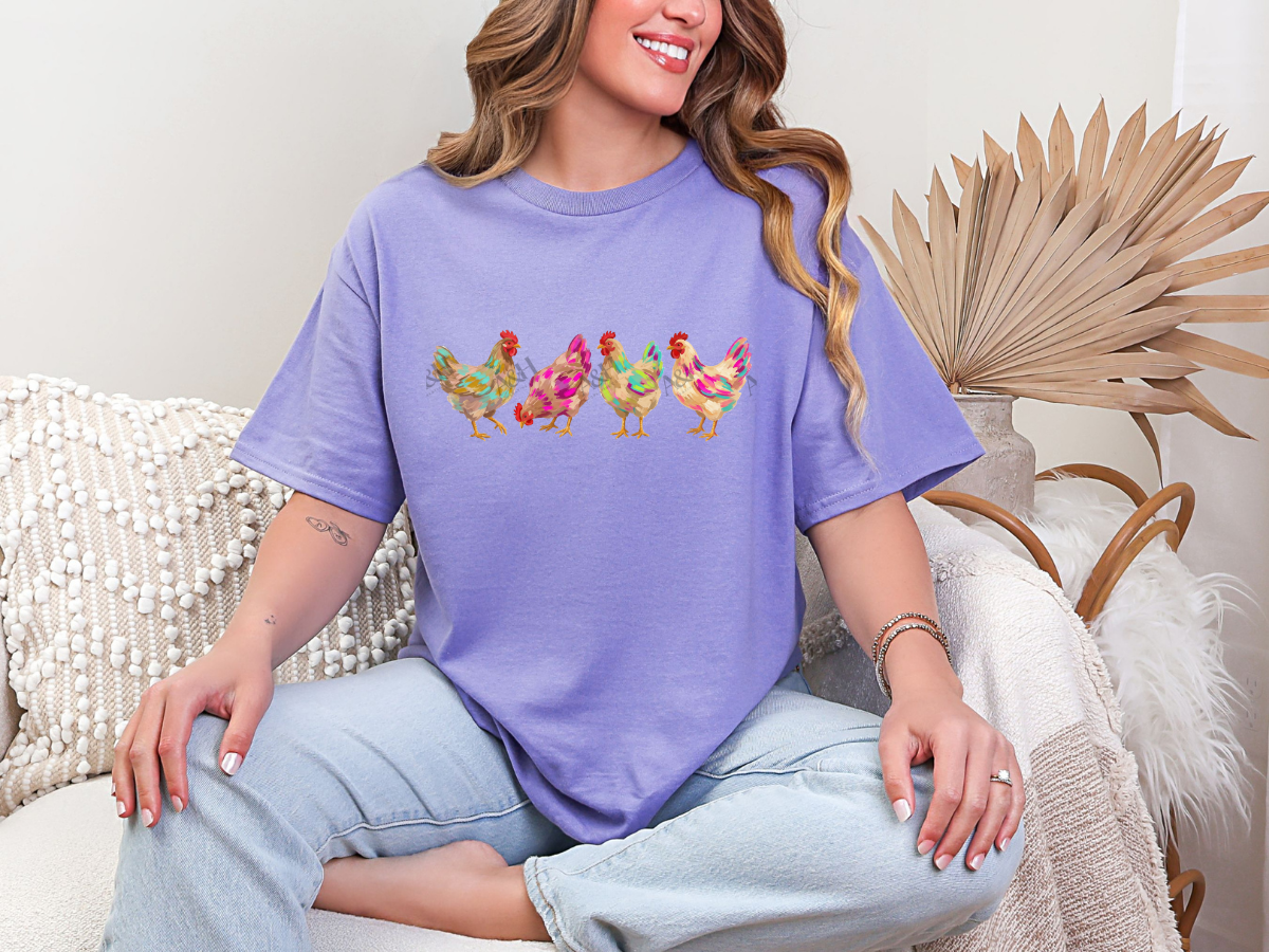 Woman wearing a purple colorful chicken graphic tee featuring four watercolor-style hens