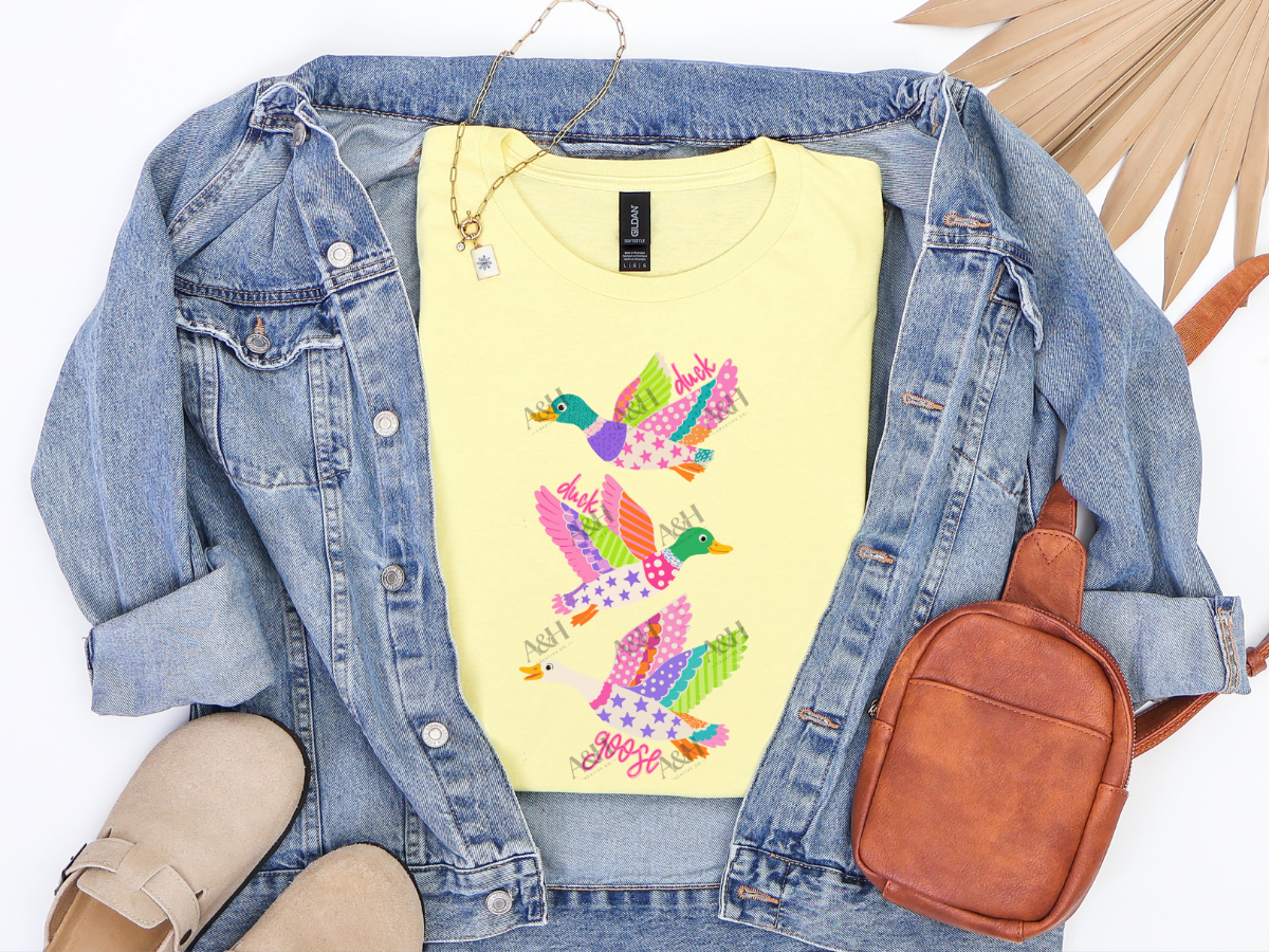 Yellow Duck Duck Goose graphic tee with colorful patterned birds styled with a denim jacket and brown accessories.