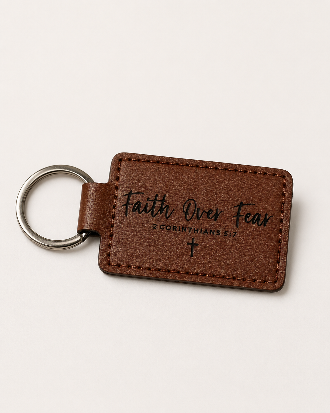 Brown leatherette keychain laser engraved with the words Faith Over Fear, 2 Corinthians 5:7, and a cross.