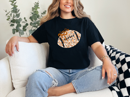 Model wearing a black Floral Football Game Day graphic tee with an orange bow and cream floral football design.