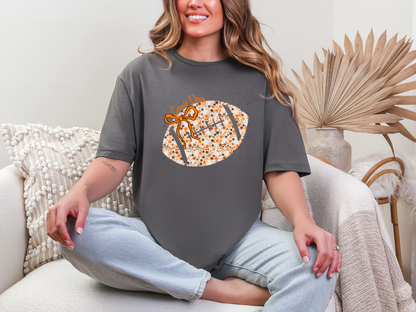Model wearing a charcoal Floral Football Game Day graphic tee with an orange bow and cream floral football design.