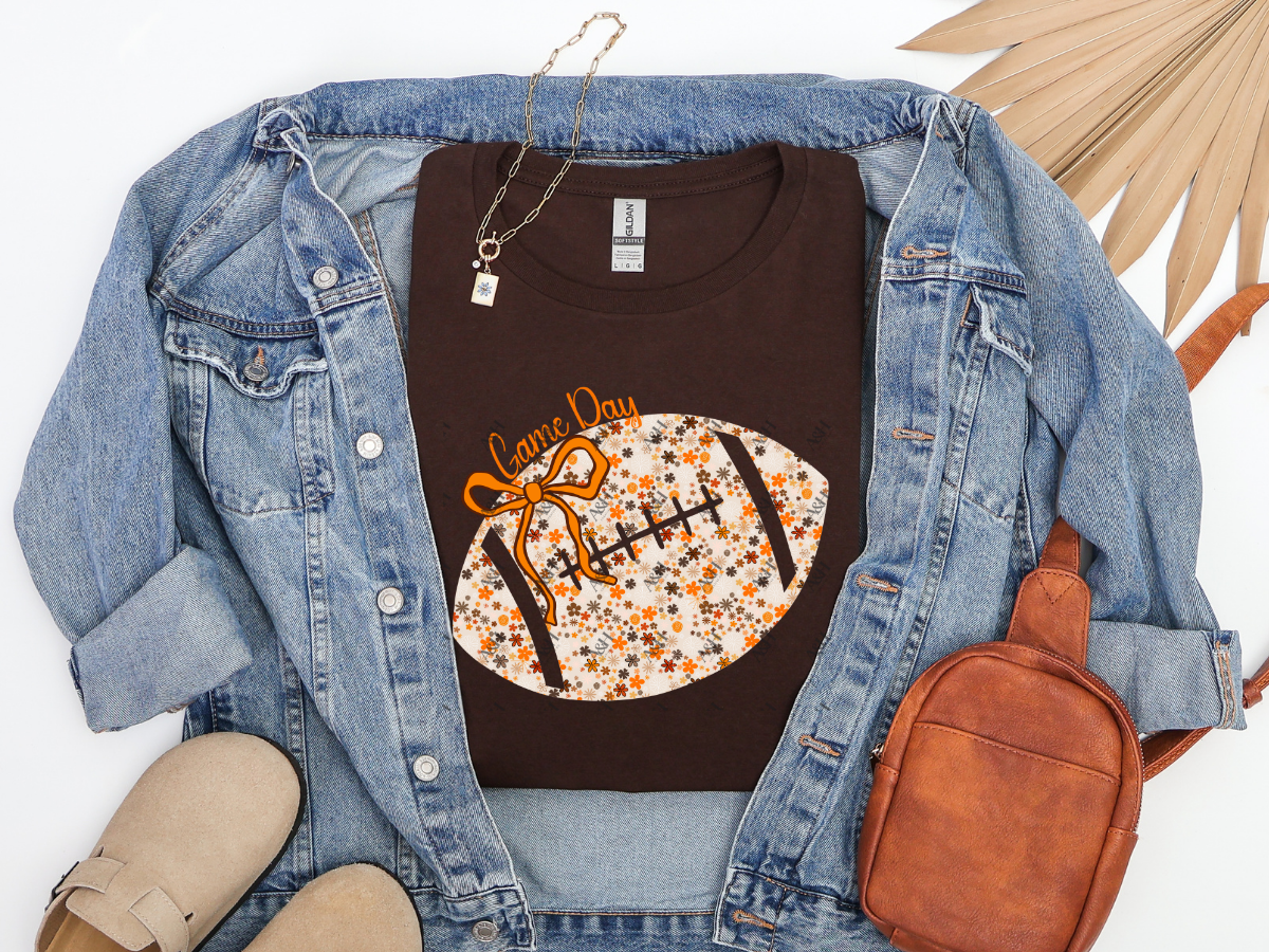 Dark chocolate Floral Football Game Day graphic tee with orange bow, styled with a denim jacket and brown accessories.