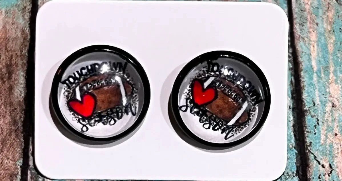Round black football stud earrings featuring brown footballs and red hearts