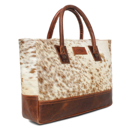 Genuine hair-on cowhide leather tote bag with brown full-grain leather trim and handles featuring a unique natural western hide pattern on a white background