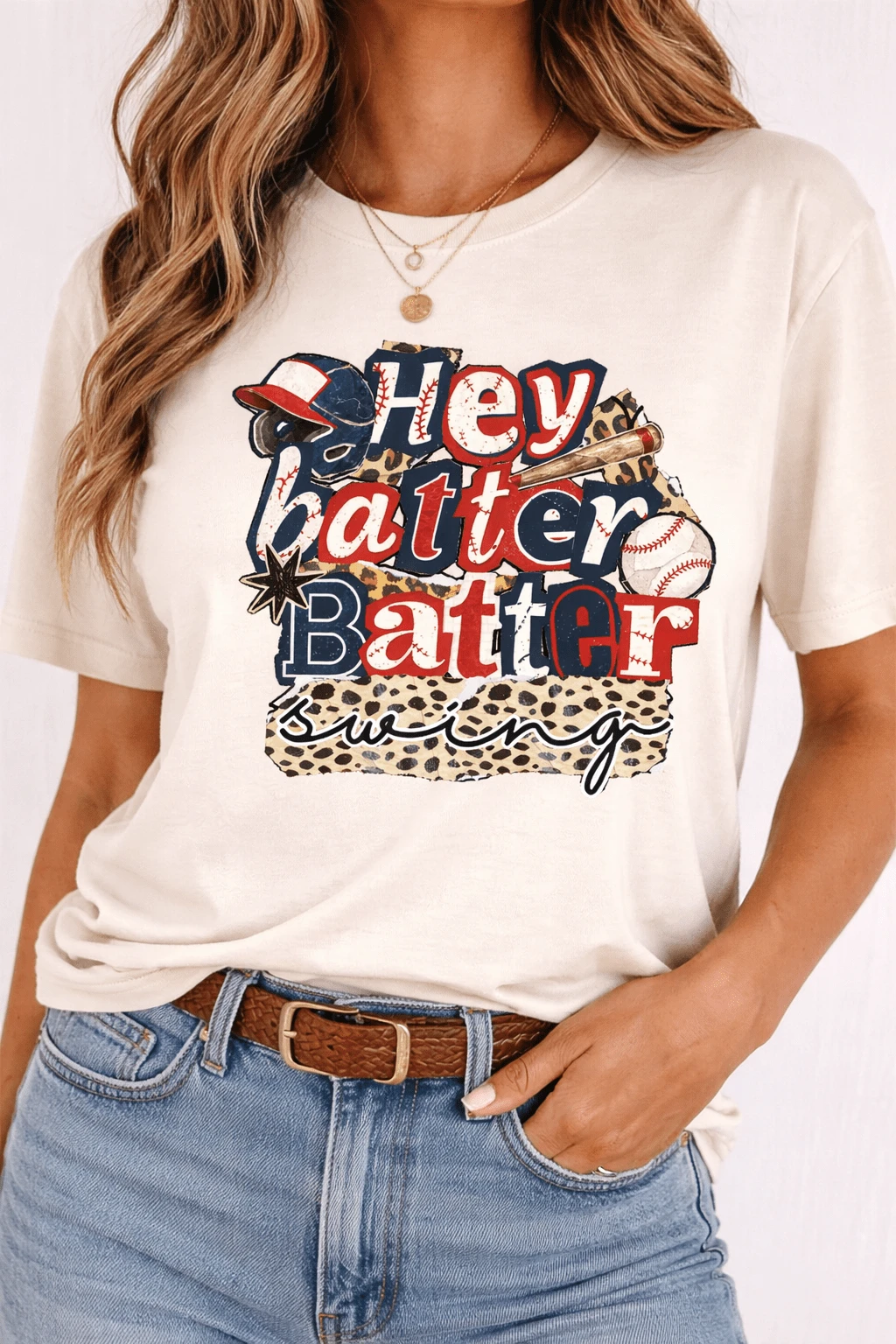 Woman wearing a cream Hey Batter Batter Swing baseball graphic tee with red, navy and leopard-print details