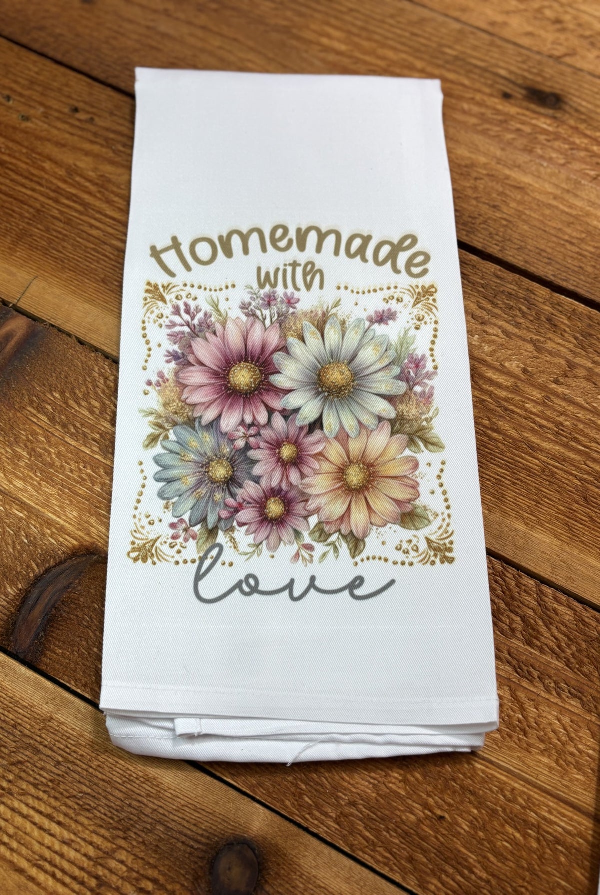 White kitchen tea towel with pastel pink, blue, and cream daisies and gold accents reading “Homemade with Love,” part of a floral tea towel set