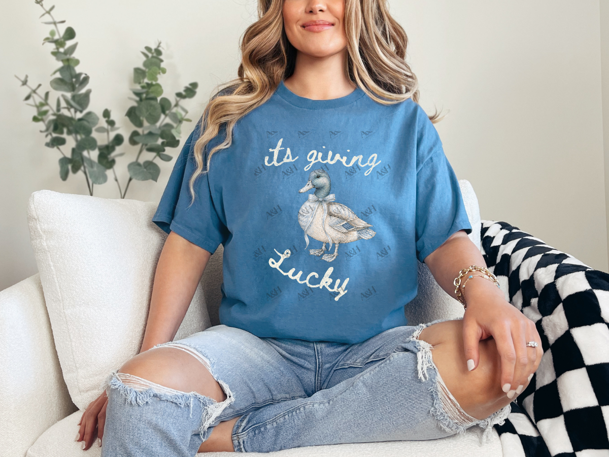 Woman wearing a blue It’s Giving Lucky duck graphic tee with a vintage-style duck illustration