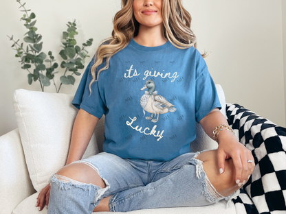 Woman wearing a blue It’s Giving Lucky duck graphic tee with a vintage-style duck illustration