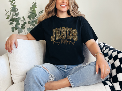 Model wearing a black Jesus John 14:6 Christian graphic tee with gold and brown leopard-print lettering.