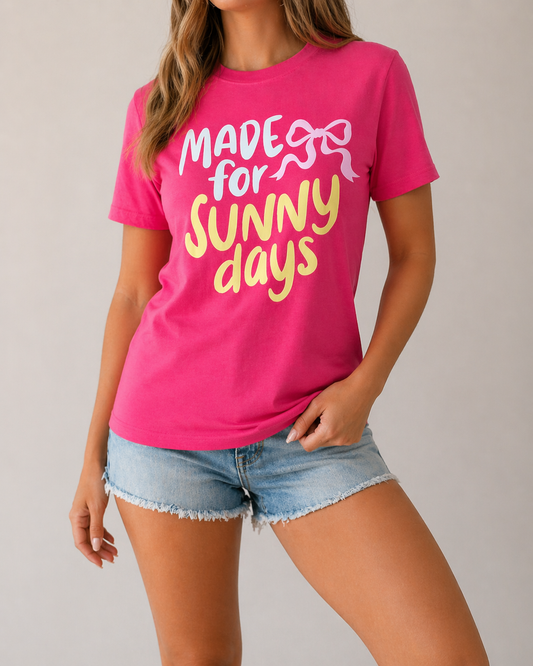 Woman wearing a bright pink Made for Sunny Days graphic tee with yellow lettering and a white bow