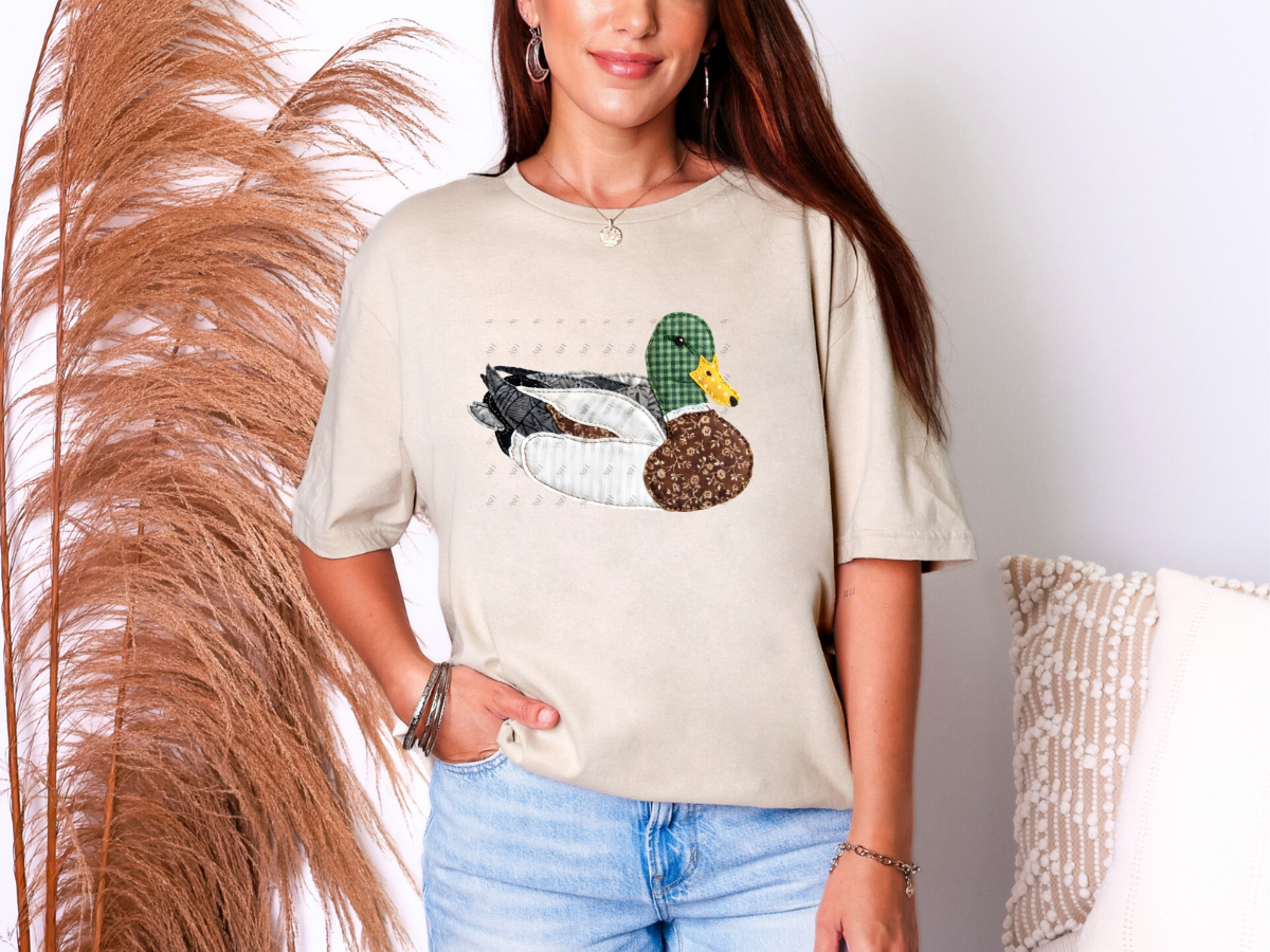 Cream graphic t-shirt featuring a vintage patchwork-style mallard duck illustration with quilt-inspired fabric textures, perfect for duck lovers and farmhouse fashion.