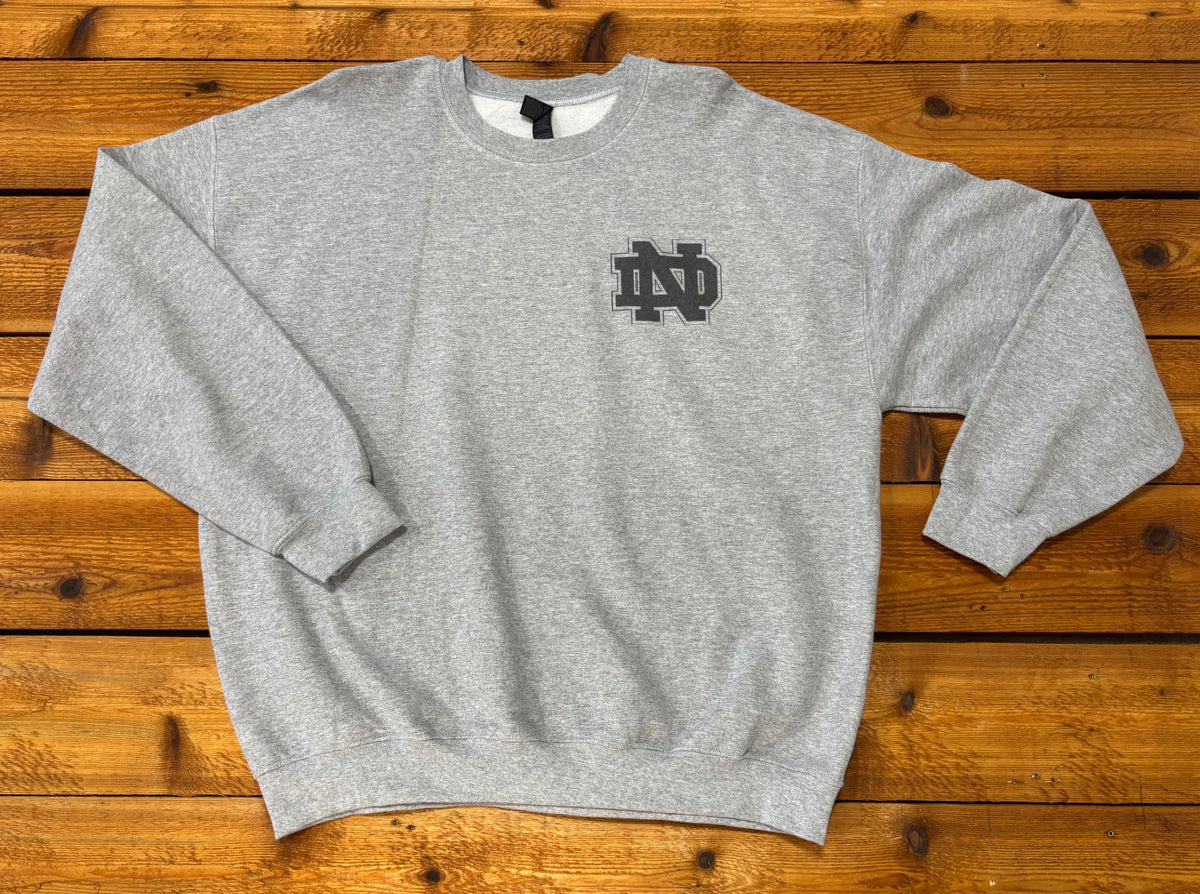 Front of a gray crewneck sweatshirt with a small black interlocking ND monogram on the left chest.