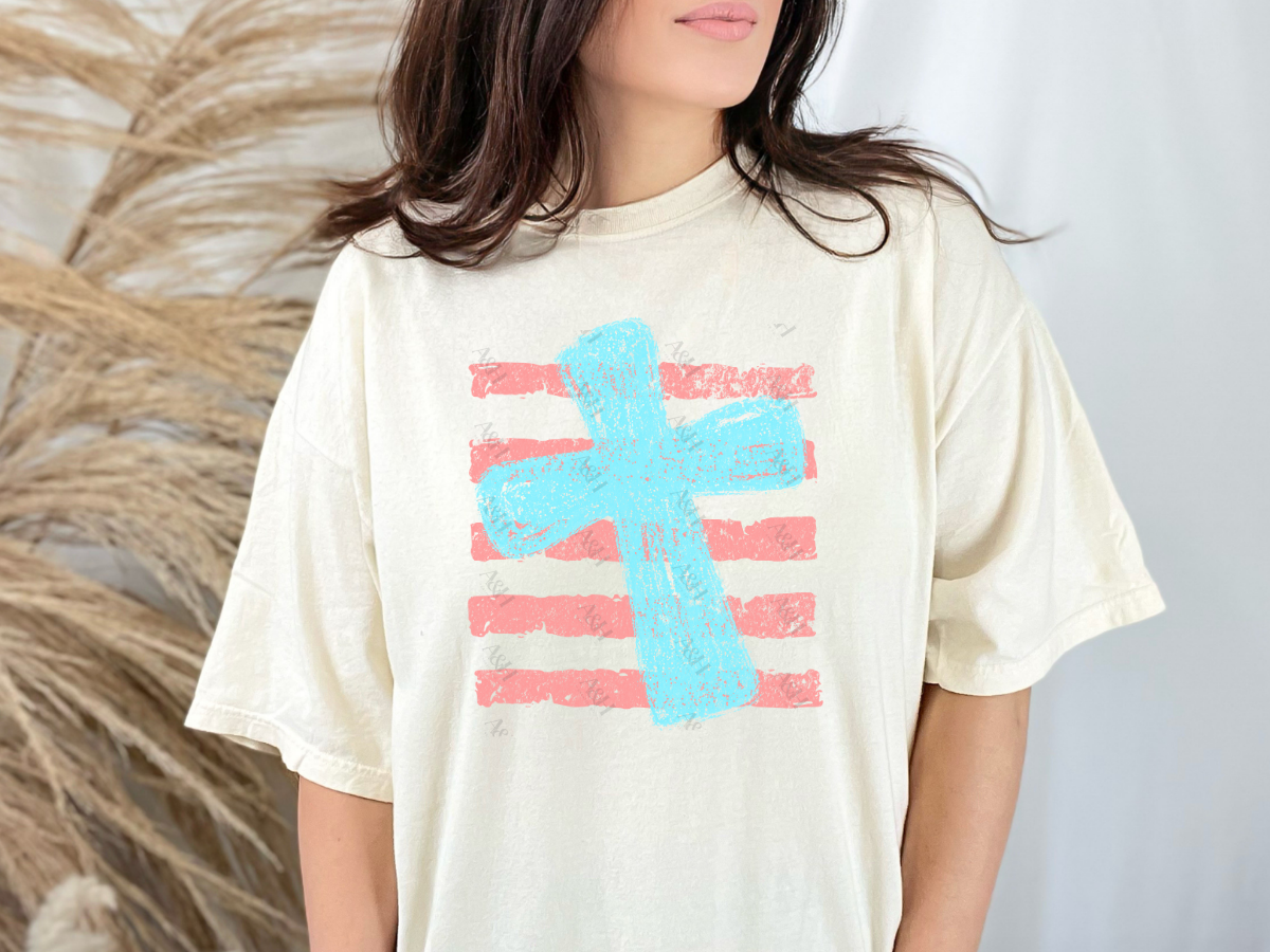 Cream Christian graphic tee featuring a distressed pink watercolor cross layered over vintage navy blue stripes in a minimalist boutique design.