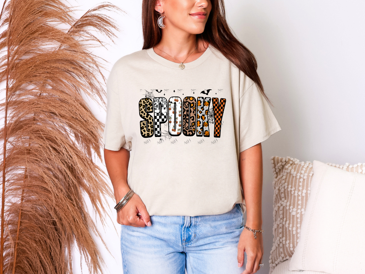Woman wearing a cream Spooky Halloween graphic tee with leopard and checkerboard lettering
