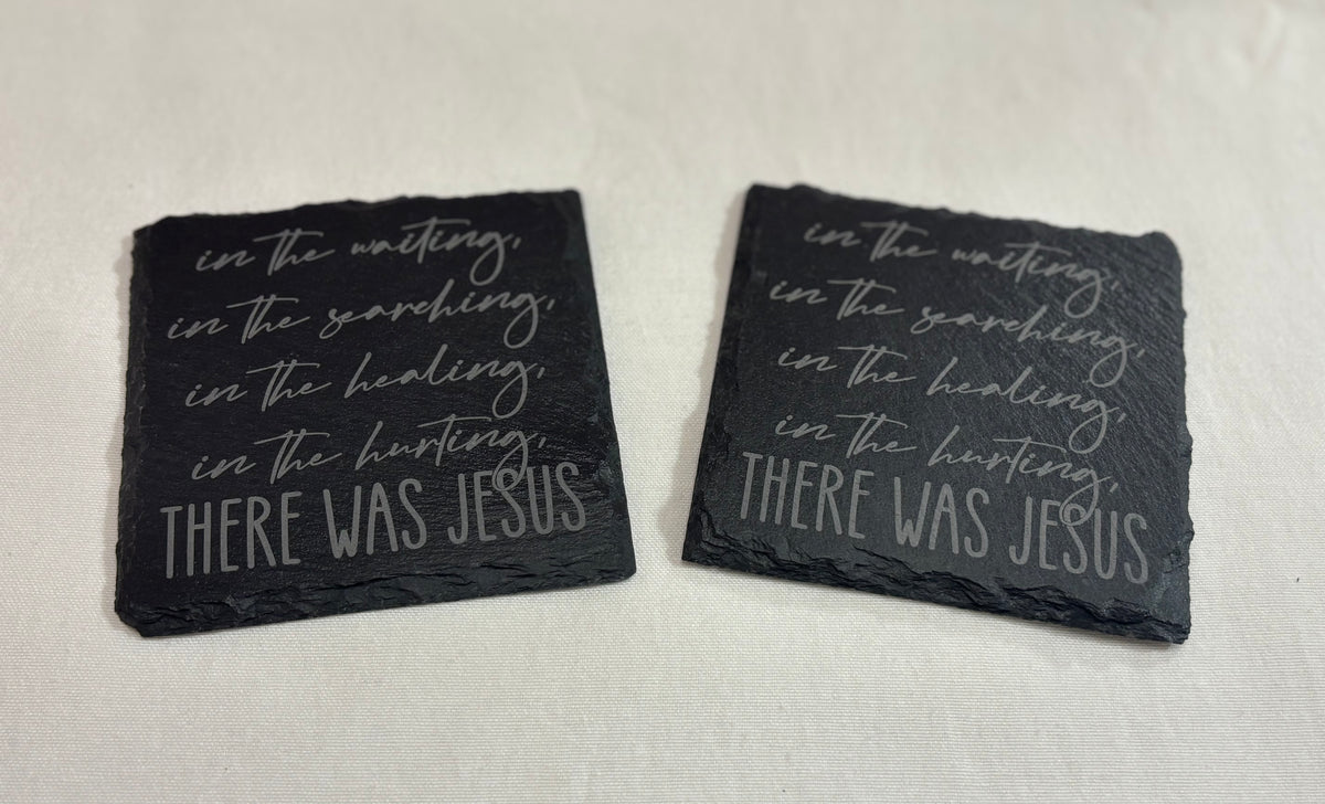 Two square black slate coasters engraved with script lettering about waiting, searching, healing and hurting, ending “There Was Jesus.”