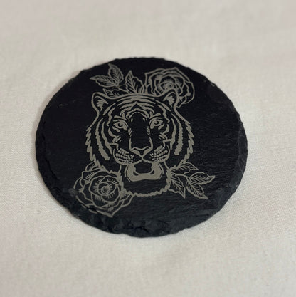 Round black slate coaster laser engraved with a tiger face framed by roses and leaves.