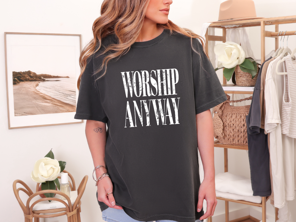 Woman wearing a pepper gray Christian graphic tee featuring distressed white "Worship Anyway" typography in a minimalist vintage design.